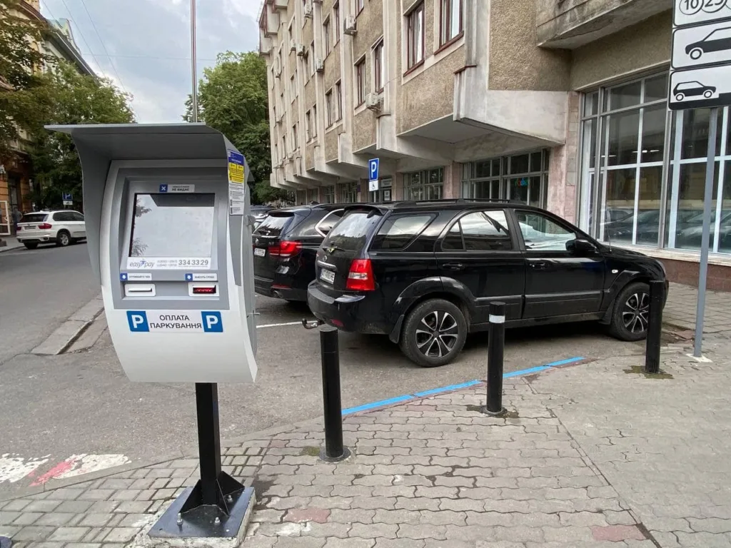 Паркомат і чорні автомобілі на парковці міста