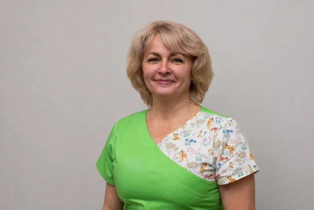 Жінка у зеленому медичному одязі посміхається