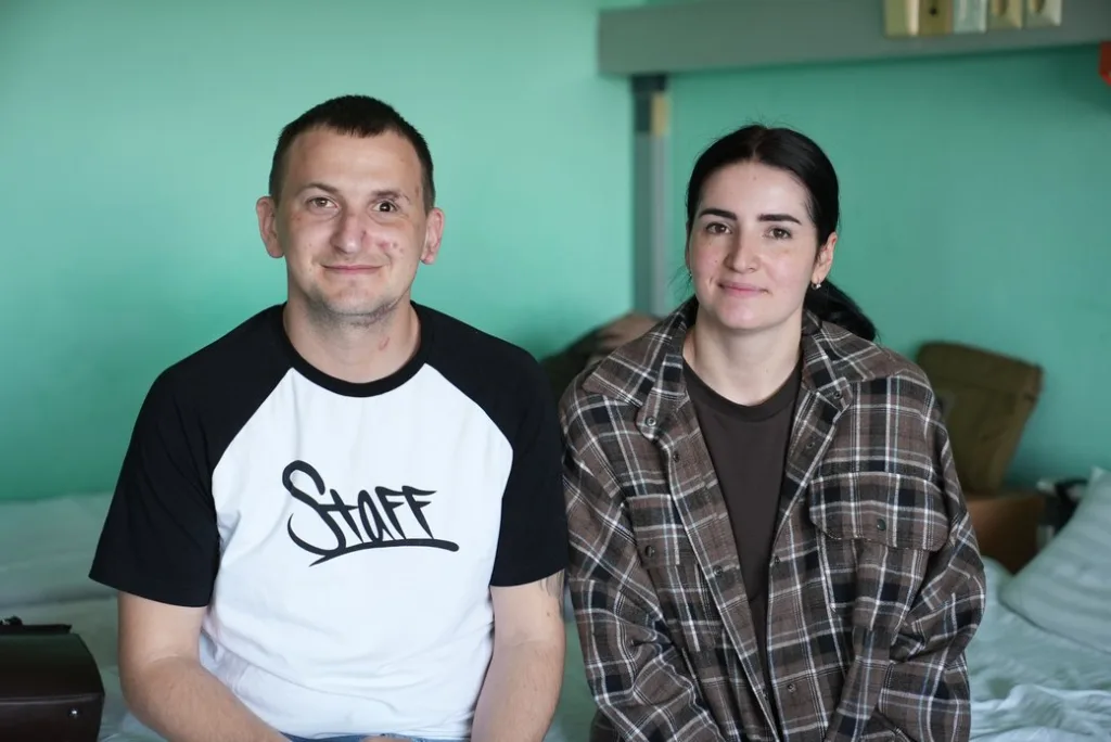 Двоє людей сидять у кімнаті та усміхаються