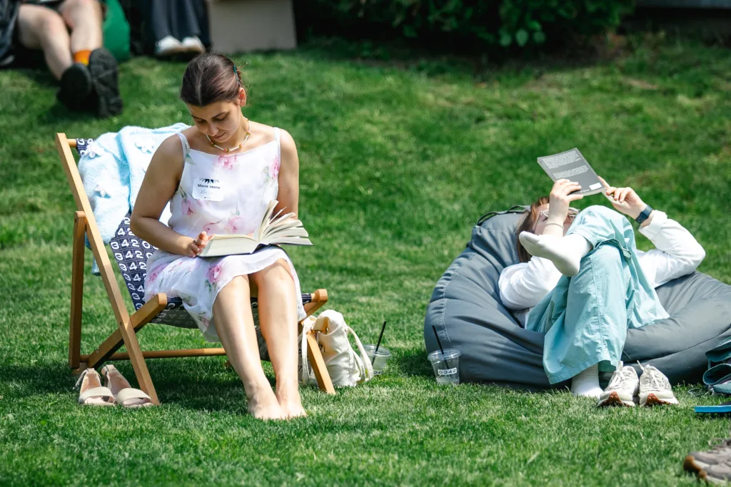 Дві жінки читають книги на траві в парку