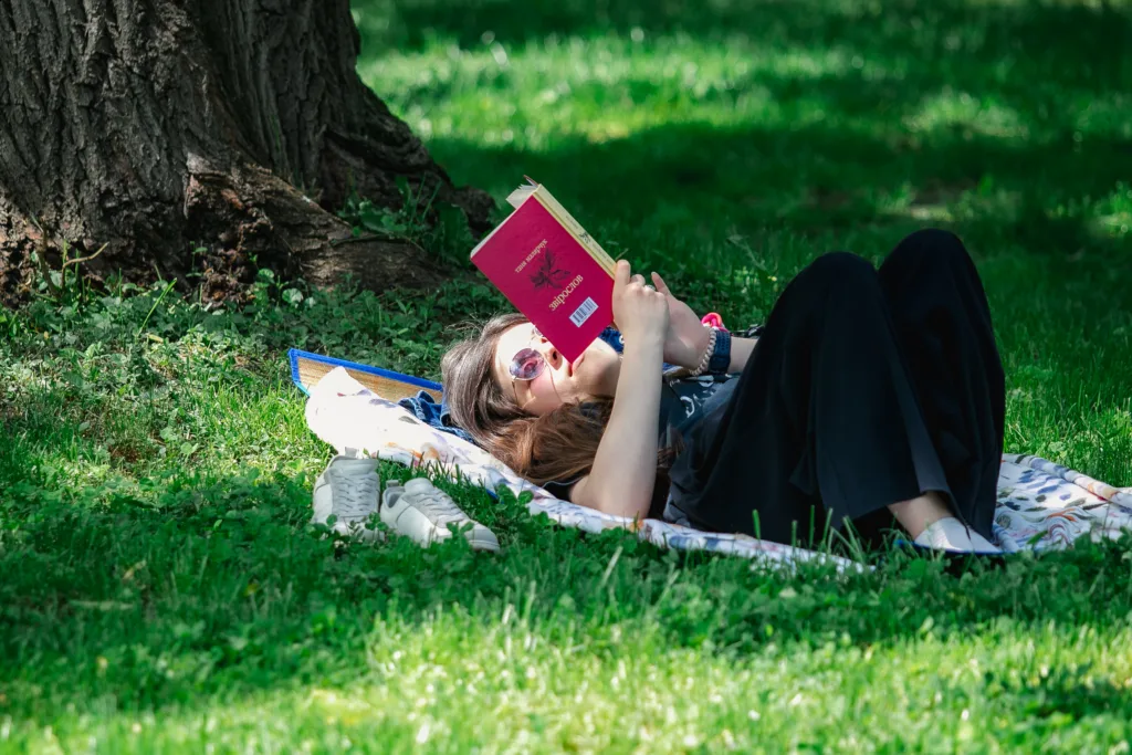 Жінка читає книгу, лежачи на траві в парку