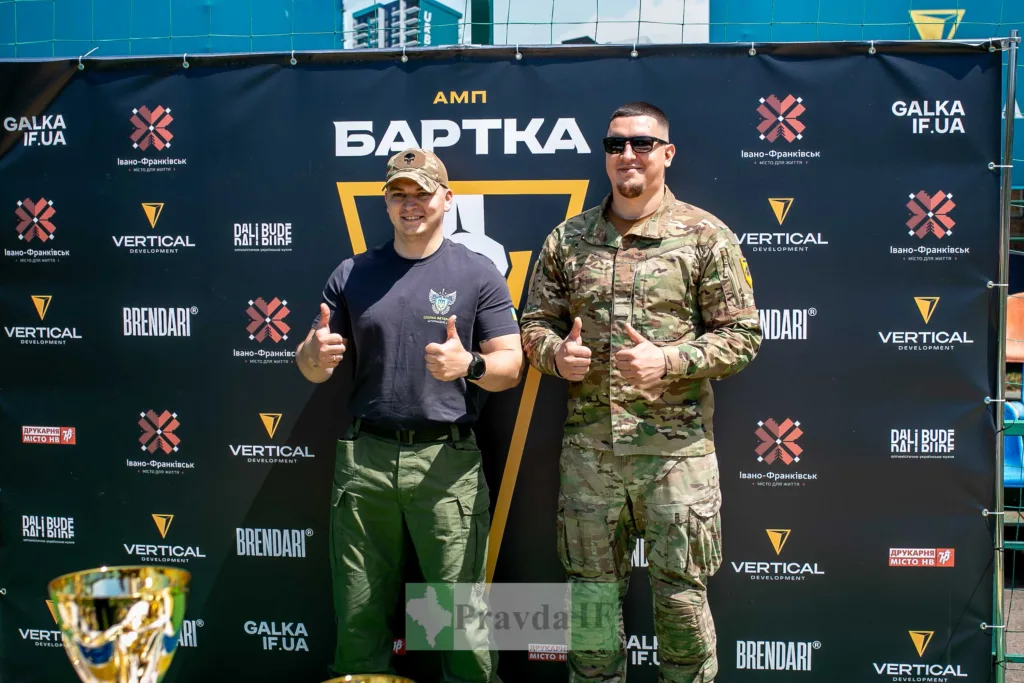 Двоє чоловіків у військовій формі на фоні банера