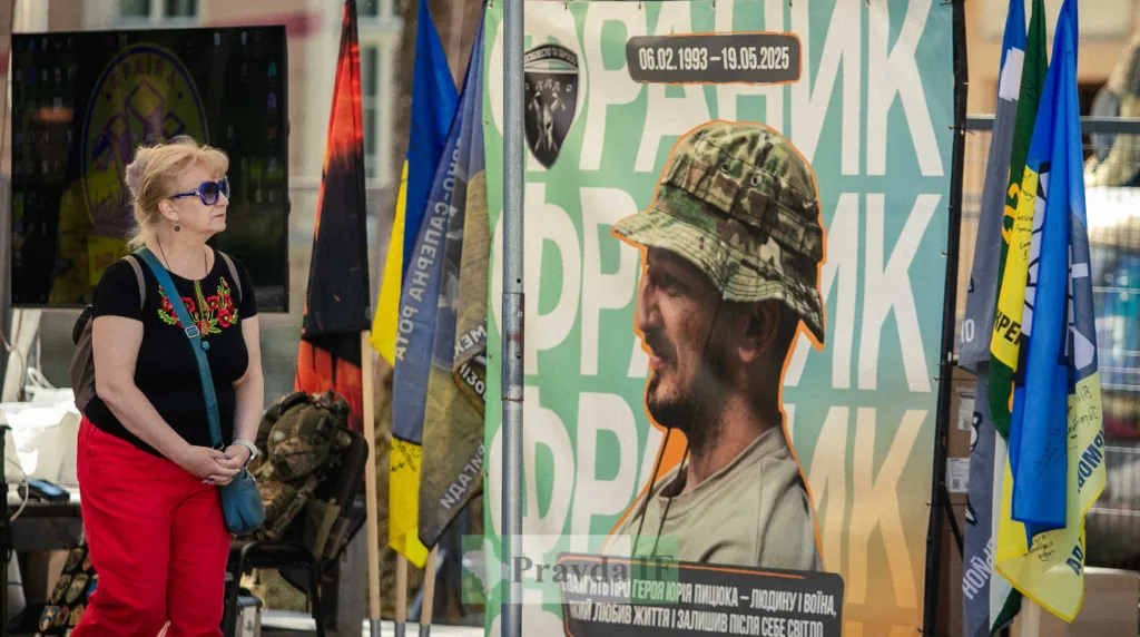 Жінка біля стенду з портретом українського військового