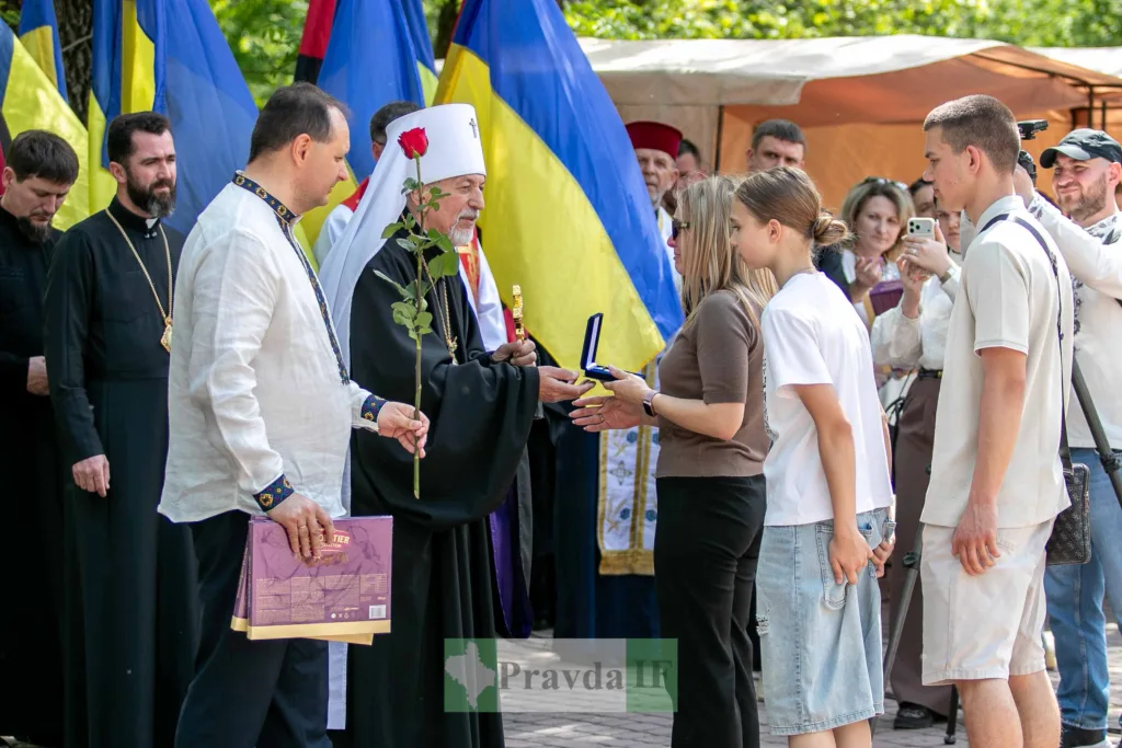 Священник вручає нагороду родині перед прапорами України