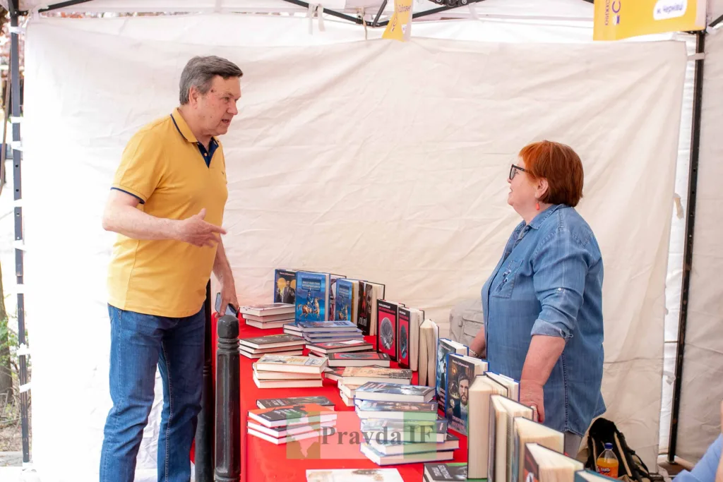 Люди розмовляють біля столу з книжками на ярмарку