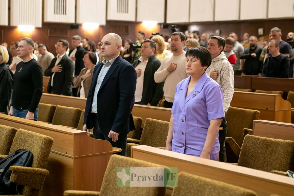 Люди стоять під час засідання у залі.
