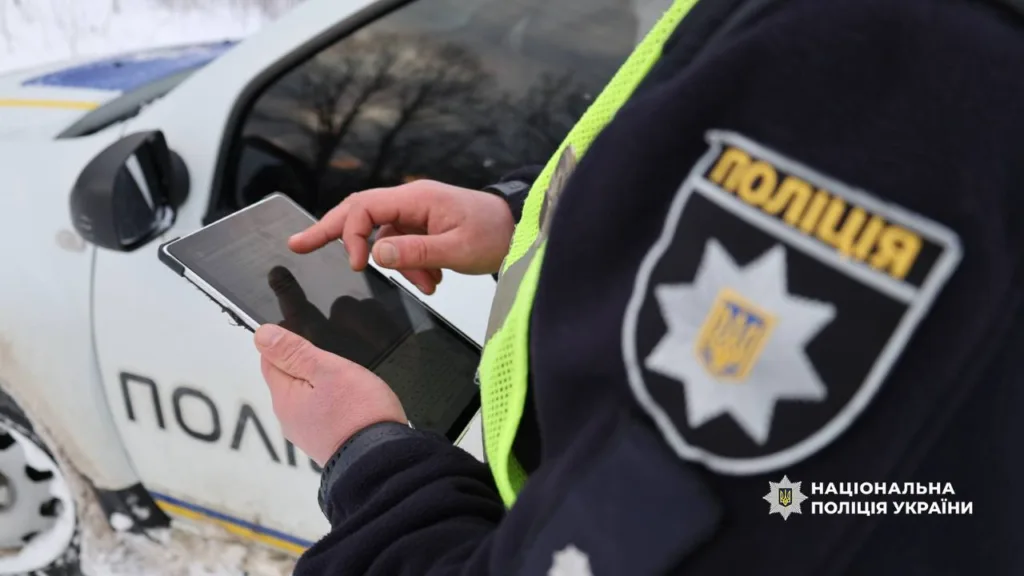 Поліцейський працює з планшетом біля патрульного авто