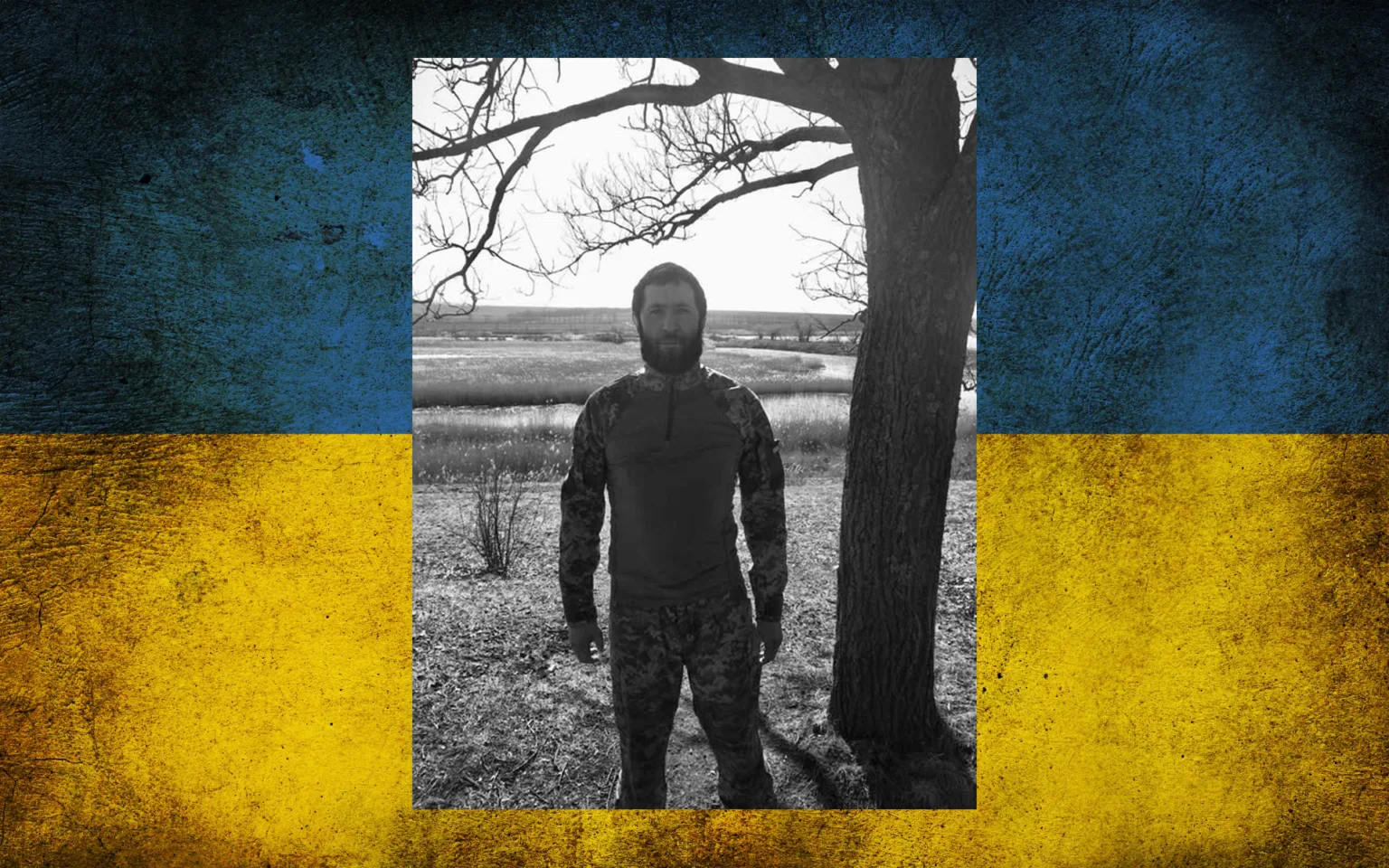 Військовий стоїть біля дерева на фоні прапора України