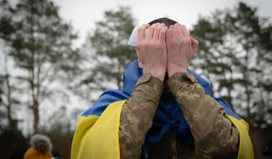Військовий з українським прапором закриває обличчя руками