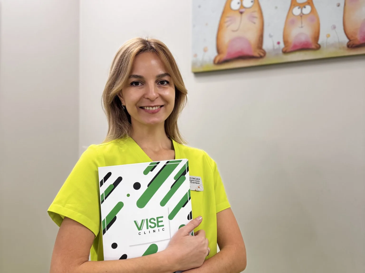 Працівниця клініки VISE посміхається, тримаючи папку