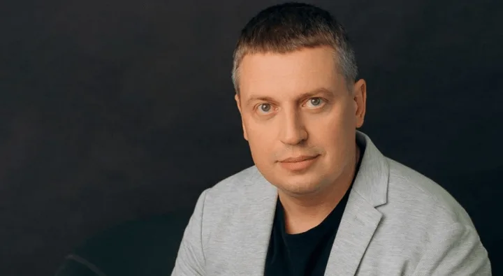 Чоловік у сірому піджаку на темному тлі