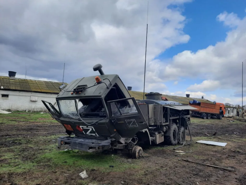 Знищена військова вантажівка на полі біля будівель