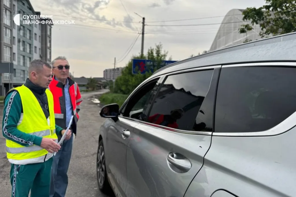 Працівники у жилетах спілкуються біля автомобіля