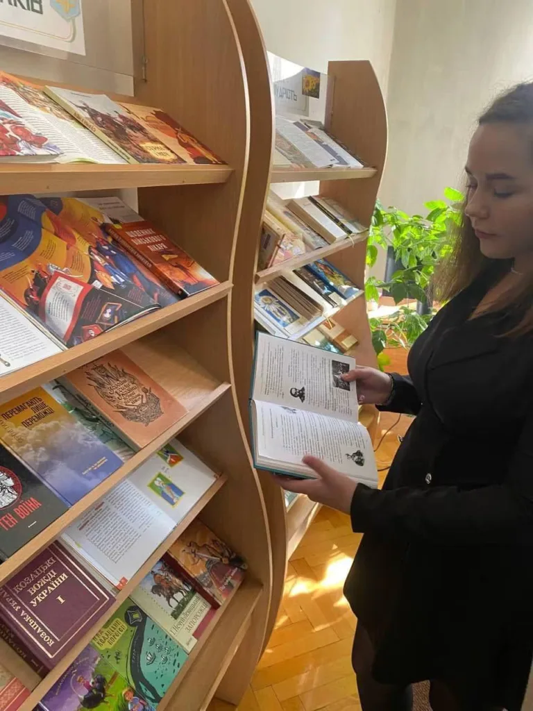 Жінка читає книгу біля полиць у бібліотеці