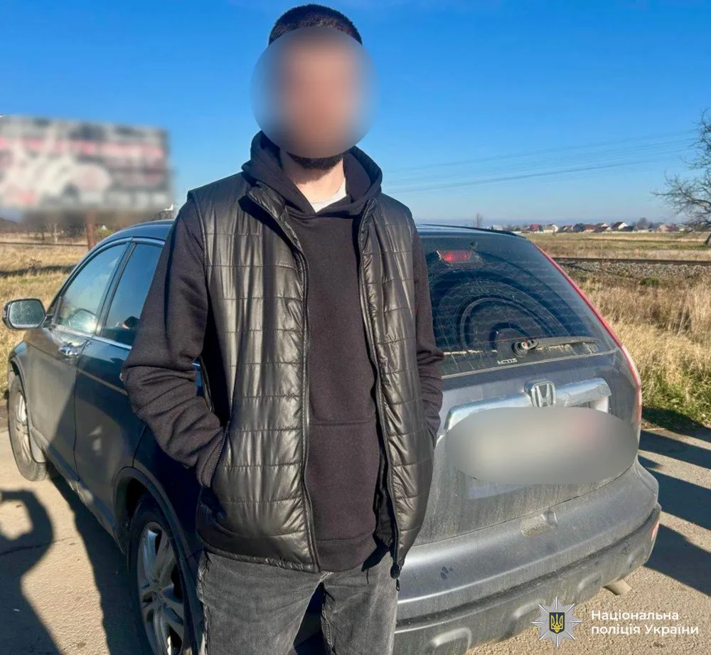 Чоловік стоїть біля сірого автомобіля Honda