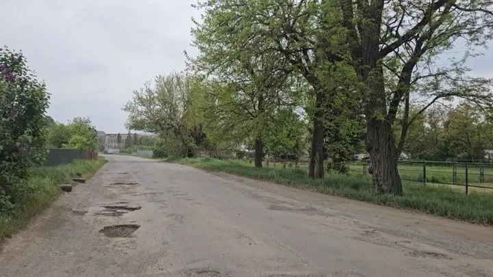 Сільська дорога з ямами та зеленими деревами