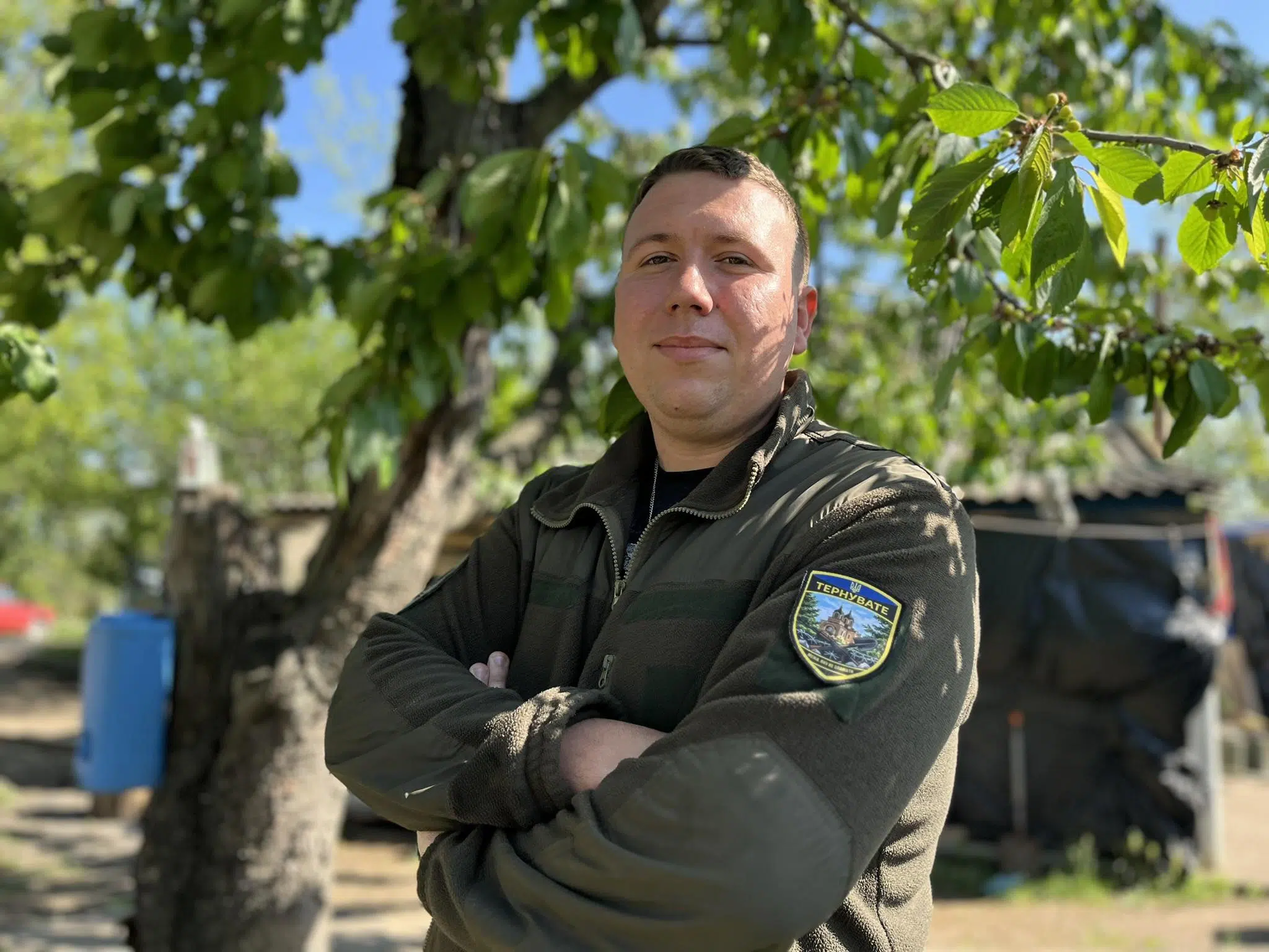 Військовий стоїть на подвір’ї серед зелені дерев