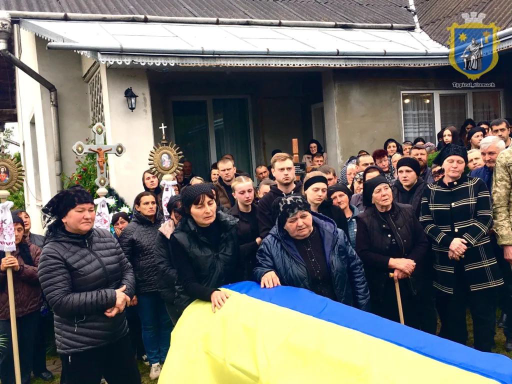 Люди прощаються із загиблим воїном під українським прапором
