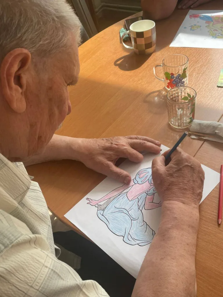 Літній чоловік розмальовує малюнок за столом