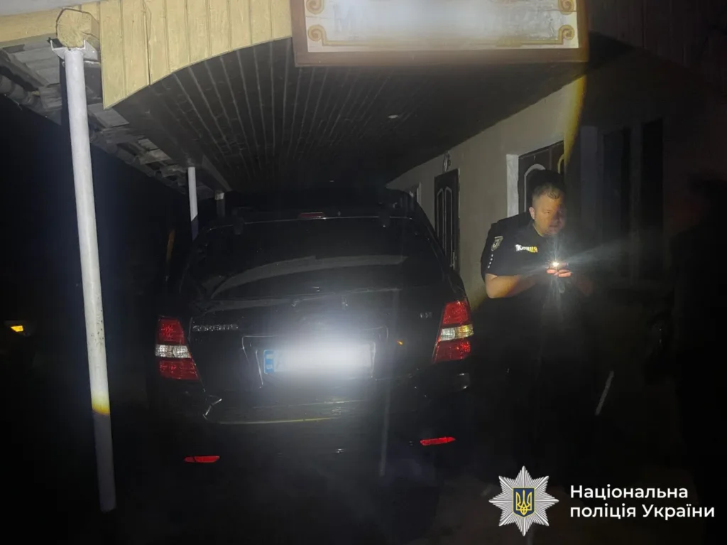 Поліцейський оглядає чорний автомобіль уночі