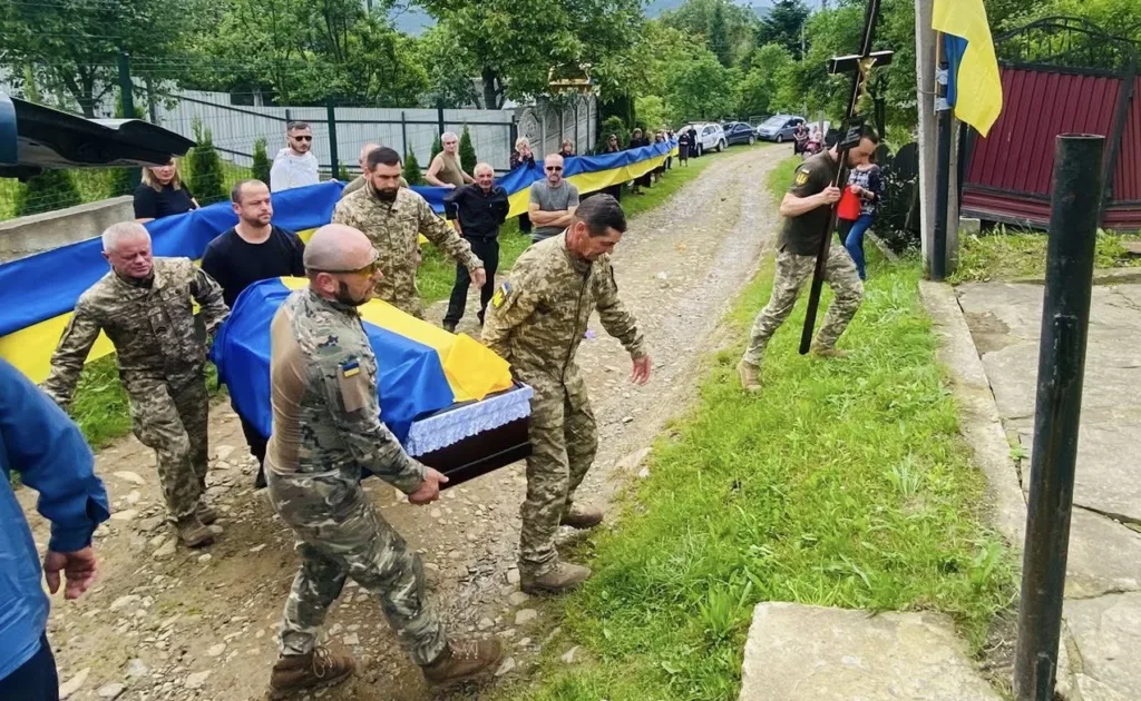 Військові несуть труну, накриту українським прапором