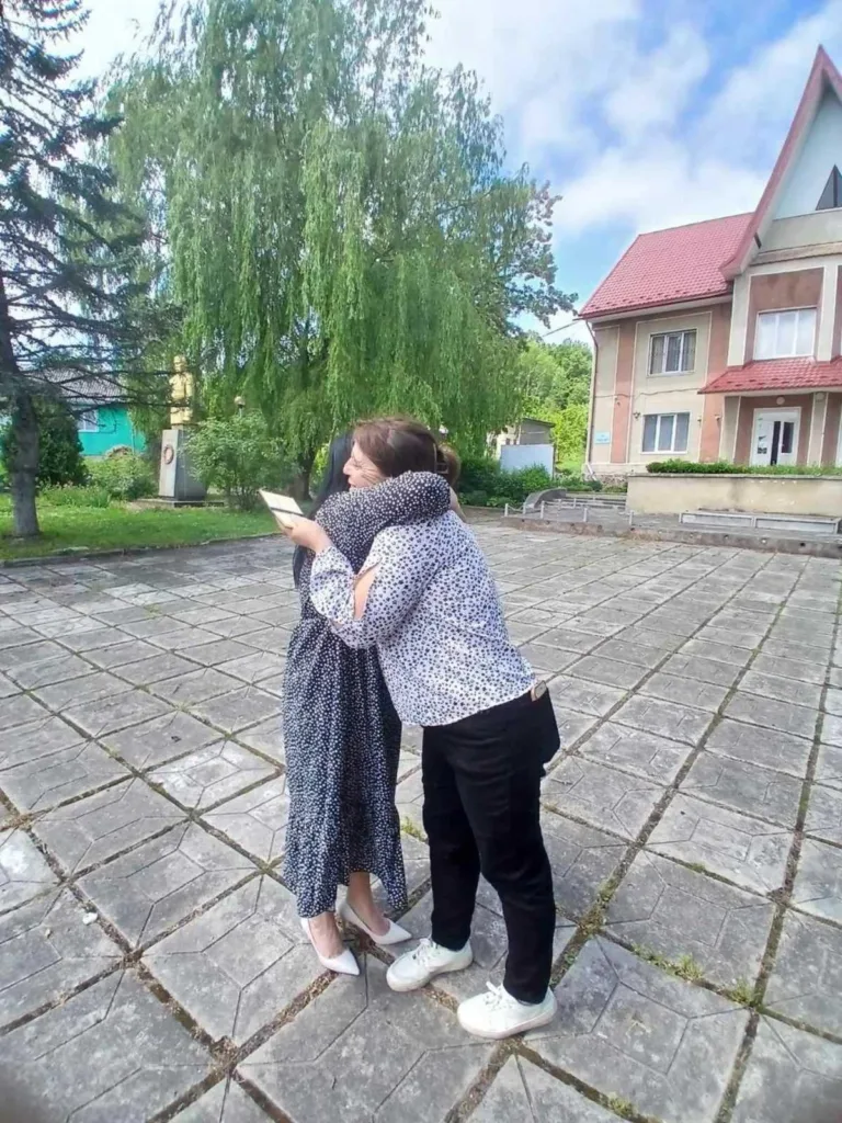 Дві жінки обіймаються на подвір’ї біля будинку