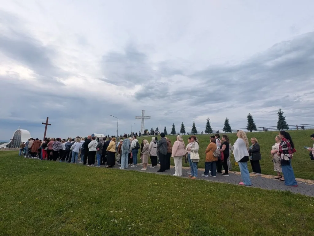 Люди стоять біля великого хреста під хмарним небом