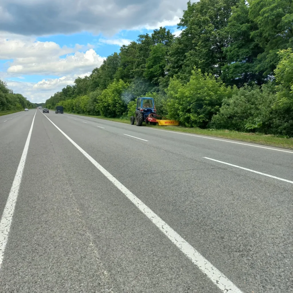 Трактор прибирає узбіччя автомагістралі біля лісу