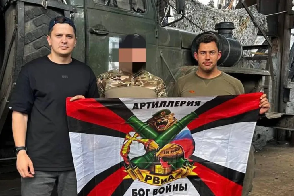 Троє чоловіків тримають військовий прапор перед вантажівкою
