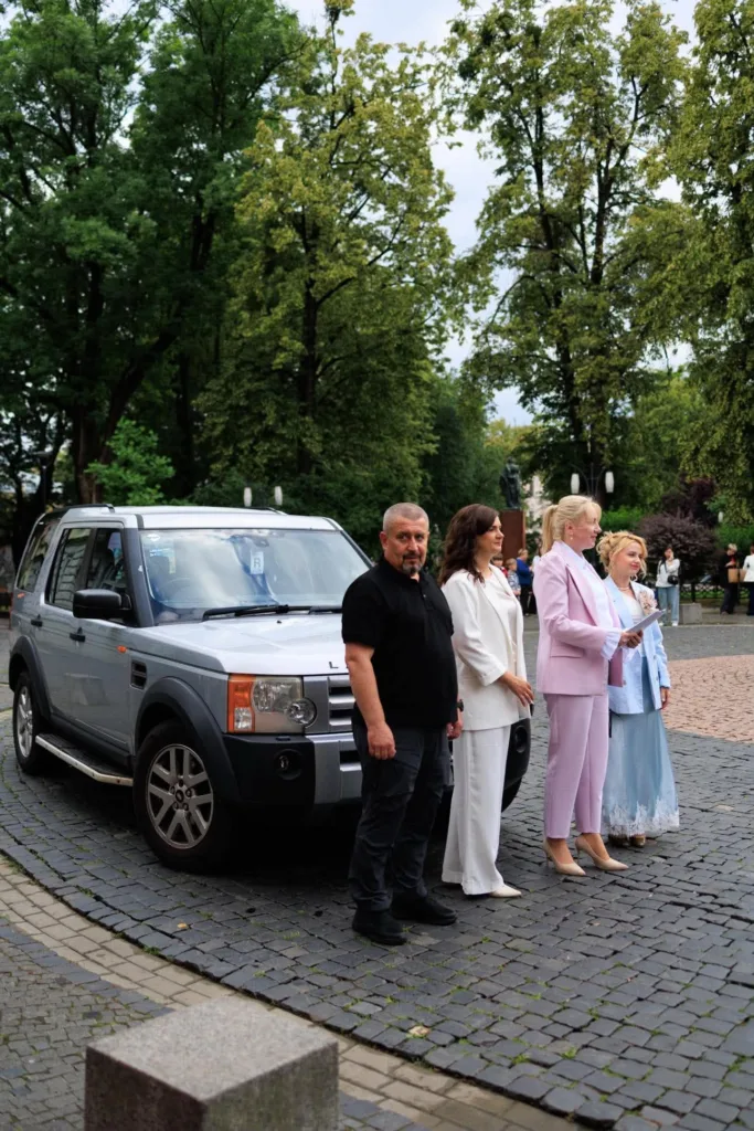 Люди стоять біля сірого позашляховика на вулиці