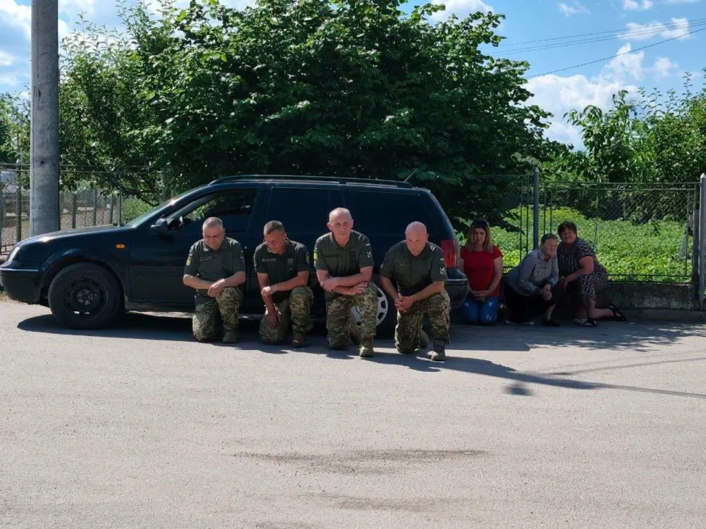 Люди на колінах біля чорного автомобіля