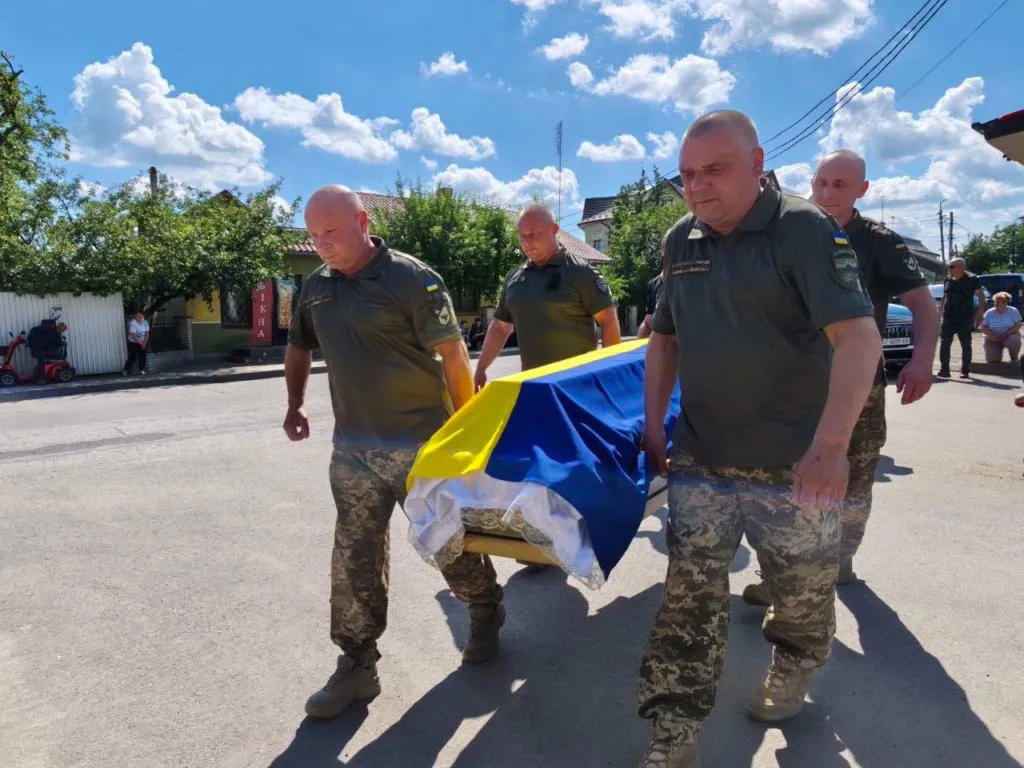 Військові несуть труну, накриту українським прапором