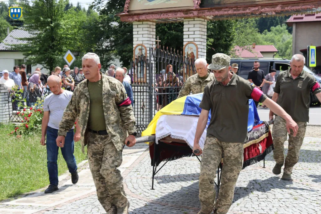 Військові несуть труну, накриту українським прапором