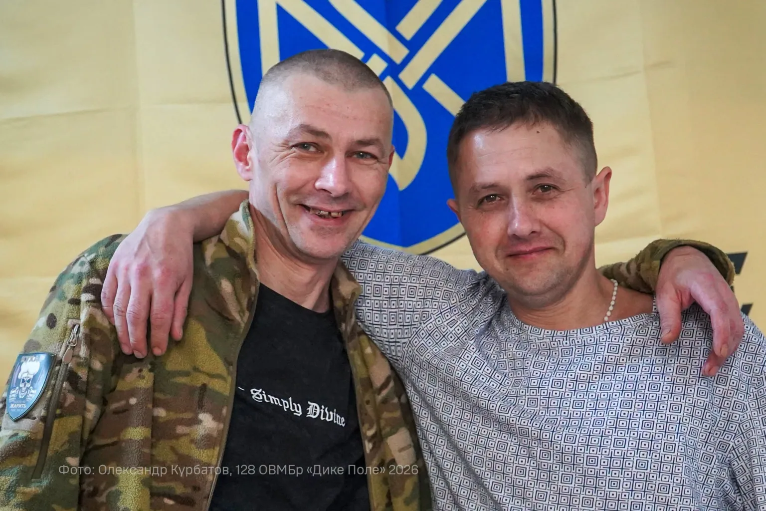 Двоє чоловіків усміхаються перед українським прапором