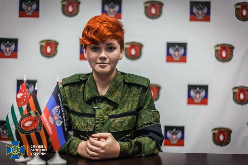 Людина у військовій формі на фоні прапорів