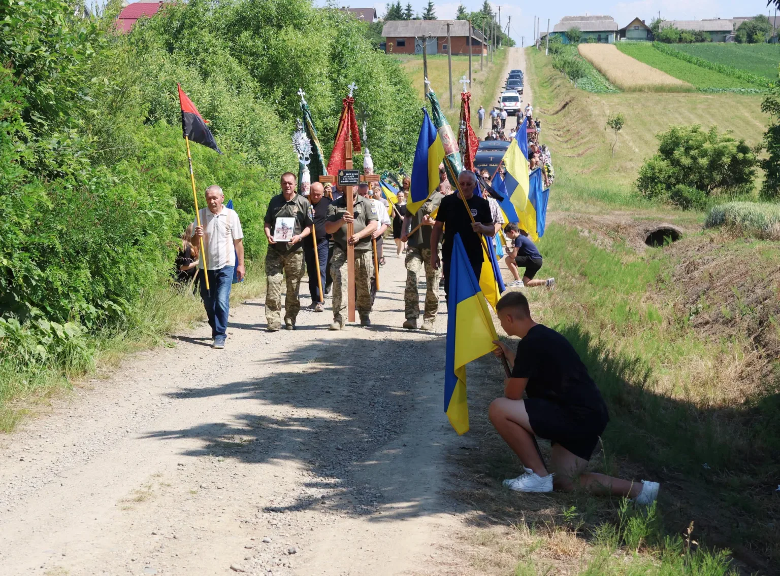 Похоронна хода з українськими прапорами на сільській дорозі