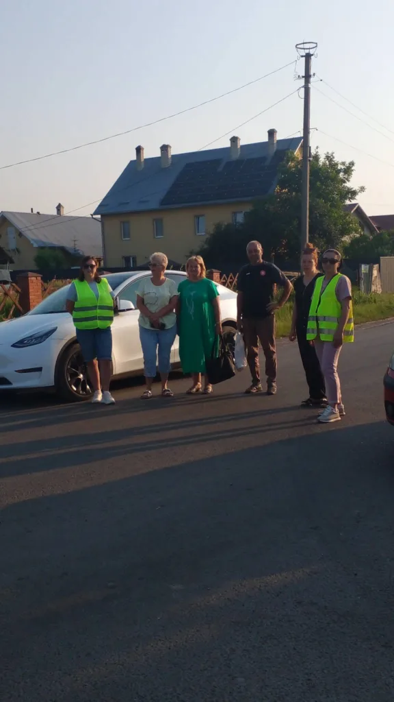 Група людей біля білого автомобіля на вулиці