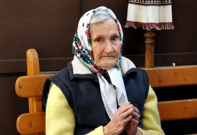 Літня жінка в хустці сидить на лавці