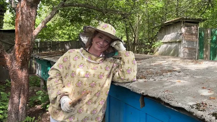 Жінка у пасічницькому костюмі біля вулика