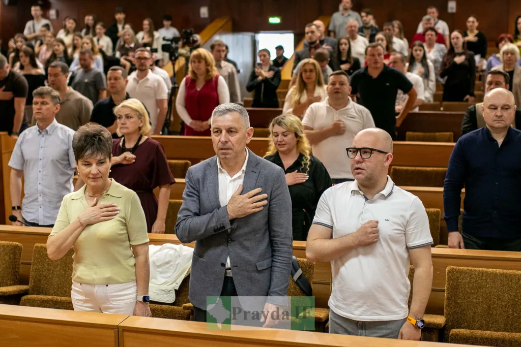 Люди стоять із рукою на серці в залі