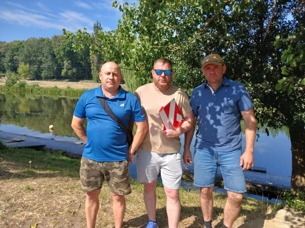 Троє чоловіків біля озера під деревами