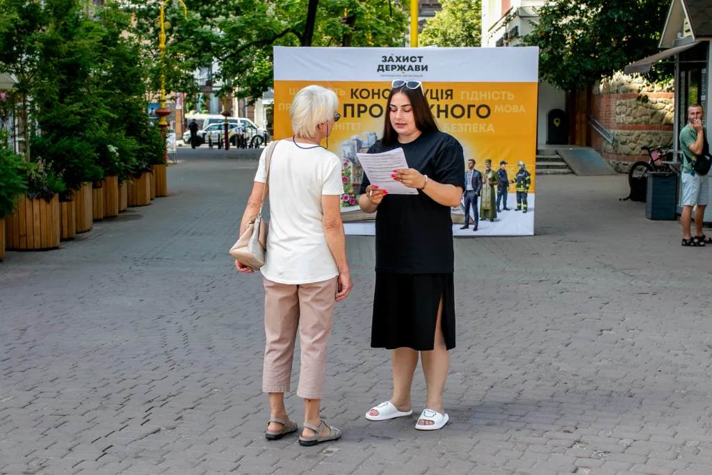 Дві жінки розмовляють перед інформаційним стендом на вулиці