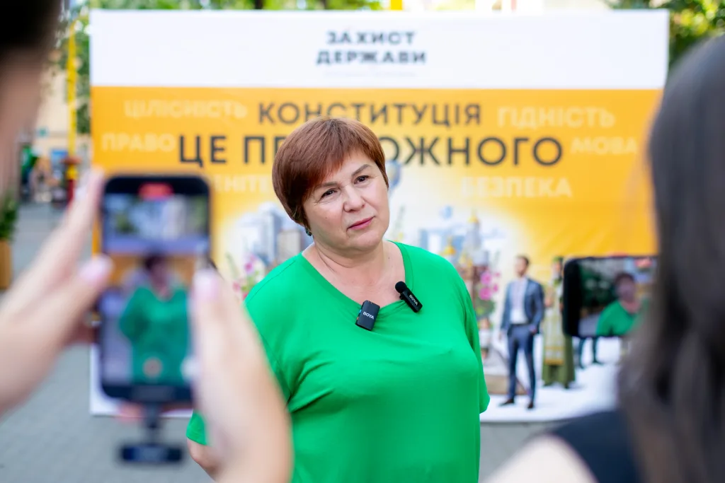 Жінка дає інтерв'ю на фоні банера про державу