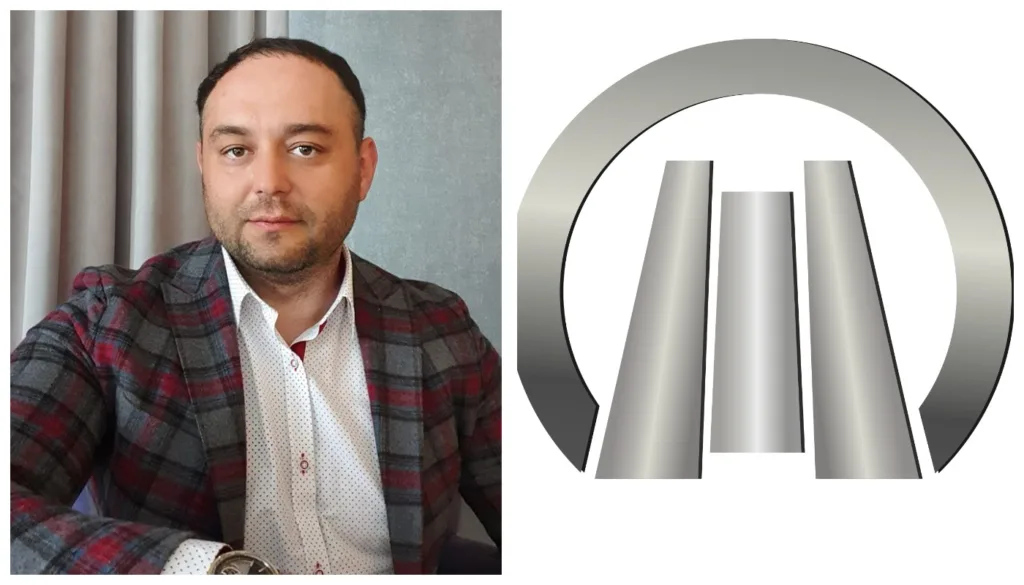Чоловік у піджаку поруч із металевим логотипом