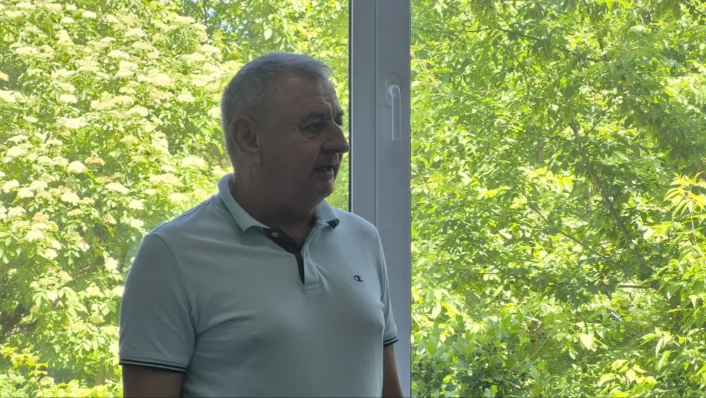 Чоловік стоїть біля вікна з зеленими деревами