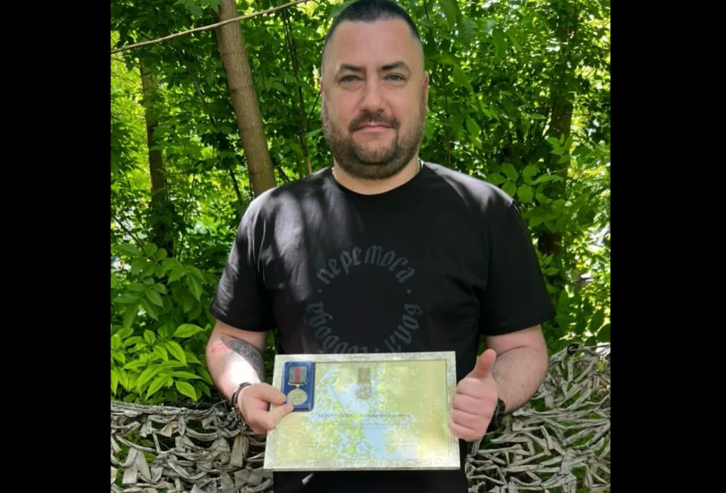 Чоловік тримає нагороду та грамоту на природі