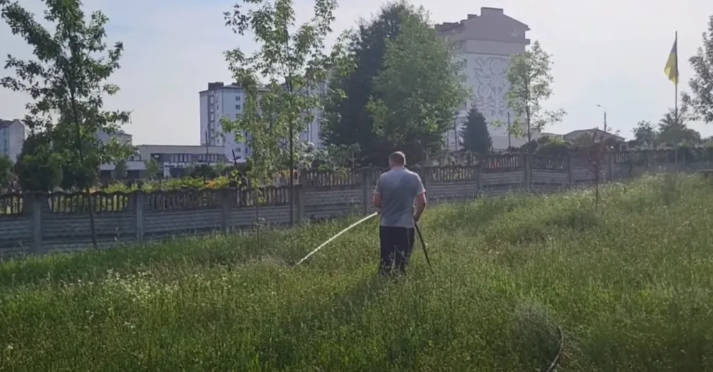 Чоловік поливає траву біля житлових будинків