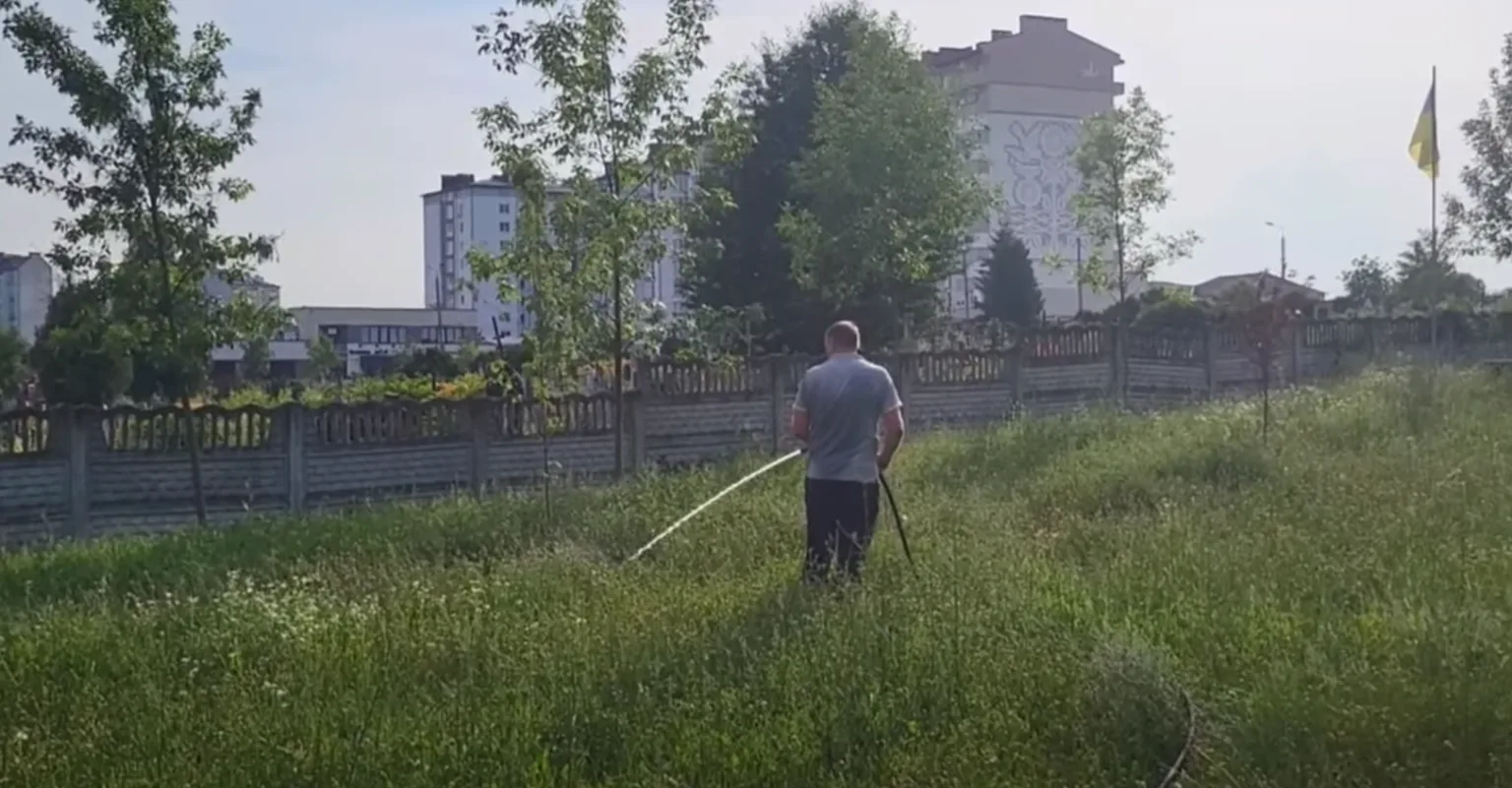 Чоловік поливає траву біля житлових будинків