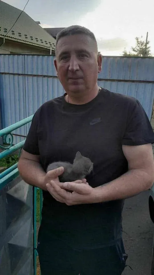 Чоловік тримає сіре кошеня на вулиці