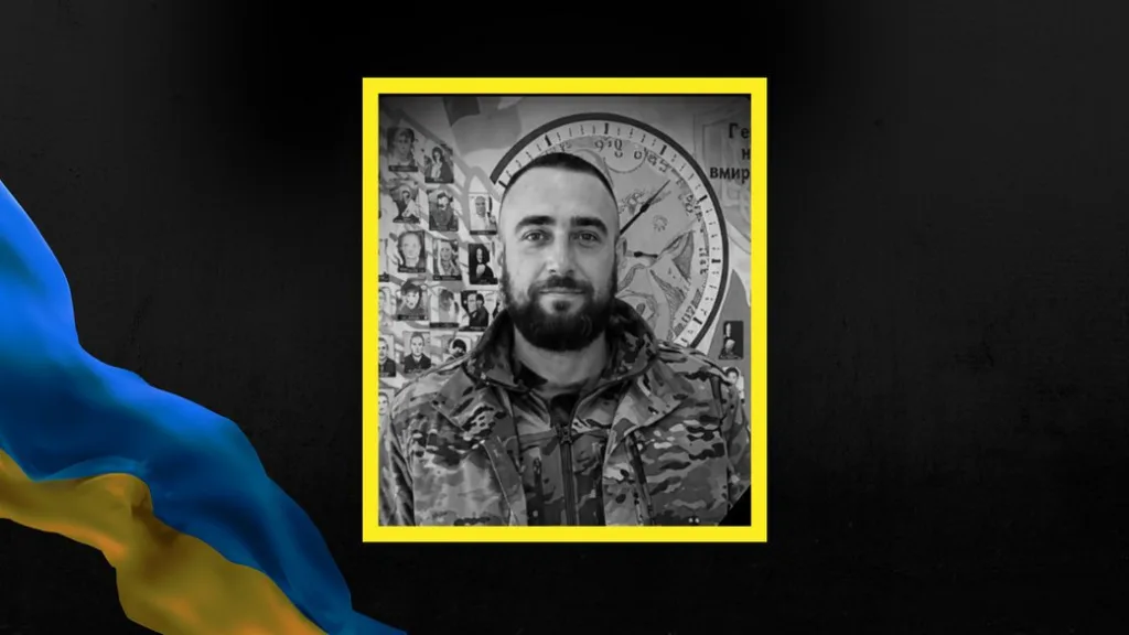 Український військовий у камуфляжі перед стіною фотографій